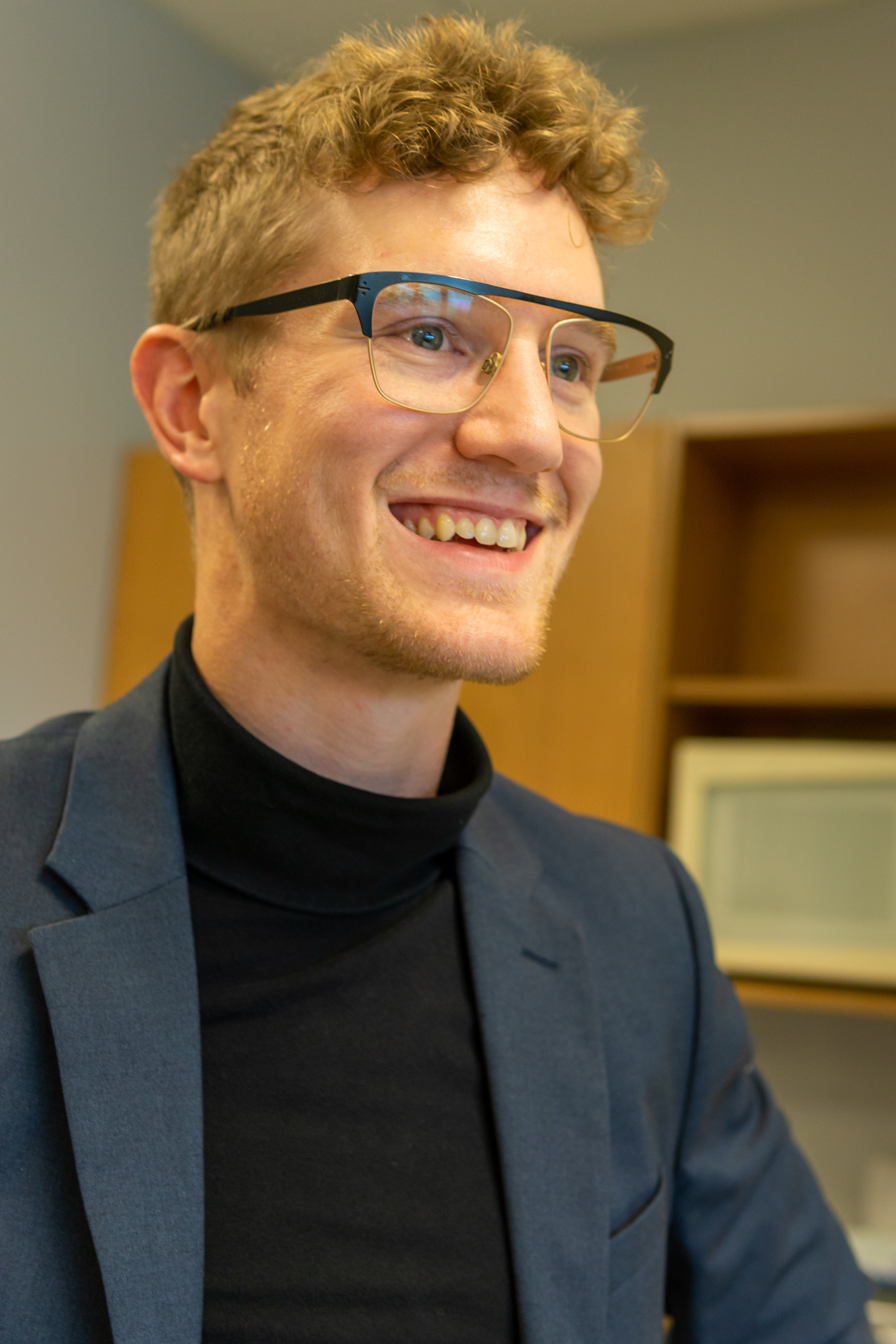 Dilan Pauli smiling in a black turtle neck shirt and glasses